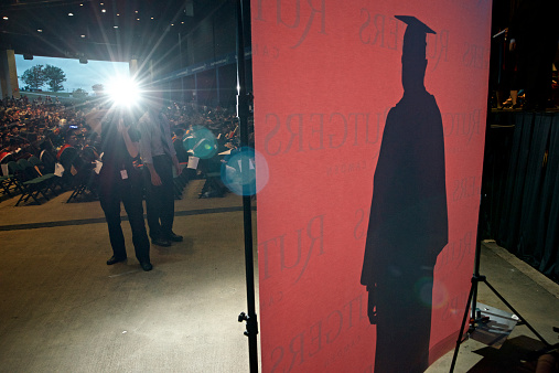 Camden, NJ, USA - May 23, 2013; Silhouette of a graduating student of Rutgers University, wearing cap-and-gown is drawn on a backdrop set up on stage as a photographer uses his flash to capture a photo. 