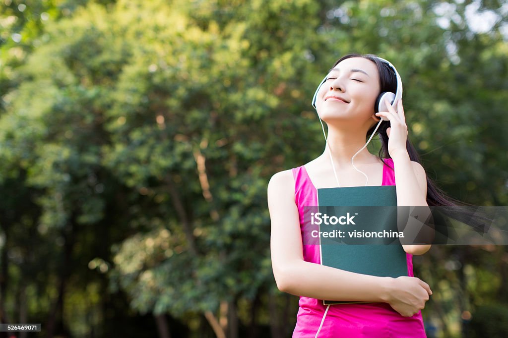 woman reading a book while listening music in park asian young woman listening music through headset and reading book in park Asia Stock Photo