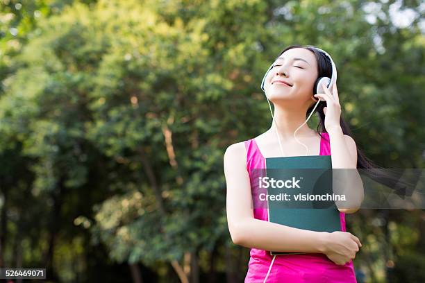 Woman Reading A Book While Listening Music In Park Stock Photo - Download Image Now - Asia, Females, Listening