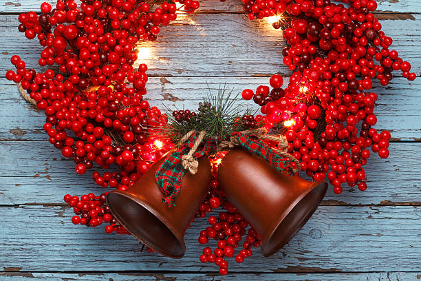 A red berry Christmas wreath with lights on old blue painted wooden planks with Christmas bells. Room for text.