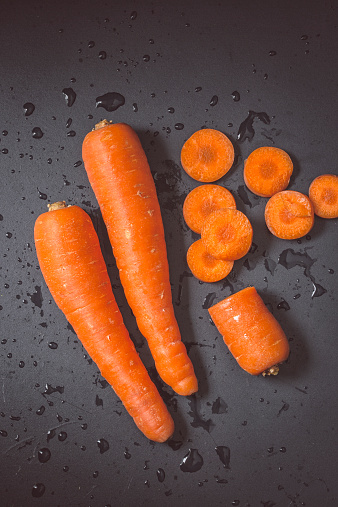 Two whole brilliant carrots and another sliced on black background.