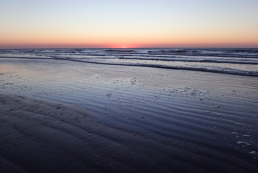 Landscape photograph of dawn on Kiawah Island, South Carolina. The sky is set, and the waves are dark blue and the ocean and the sun are orange and the sky is an orange yellow.                                                         