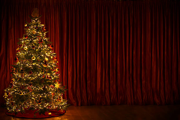 istock Lit Christmas Tree against Red Curtain Background in Dark Room 526493447