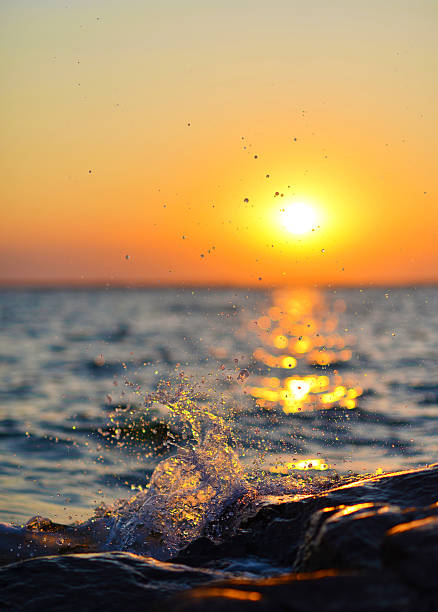 Water Splashing on Shore against Glittering Sunset Splashing water on rocks in front of golden sunset åland islands stock pictures, royalty-free photos & images