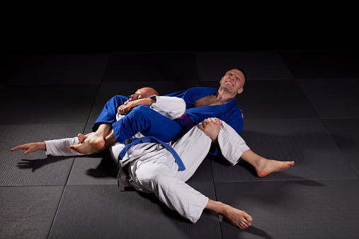 Two jiujitsu wrestlers sparring in combat during the sport training. One fighter applying joint-lock and chokehold to defeat the opponent. 