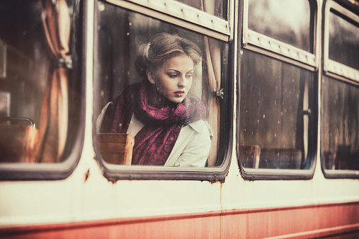 Retro styled portrait of a beautiful young woman sitting in a vintage train wagon.