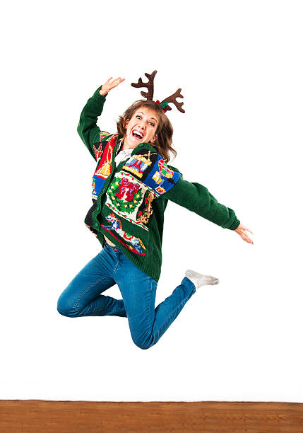 Jump for joy A young woman in a holiday sweater and antlers jumps for joy. Vertical image with copy space. christmas ugliness sweater nerd stock pictures, royalty-free photos & images