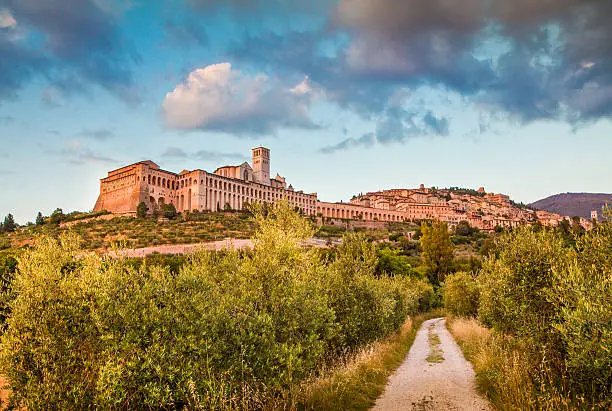 Beautiful view of the ancient town of Assisi with dramatic cloudscape in golden evening light, Umbria, Italy.