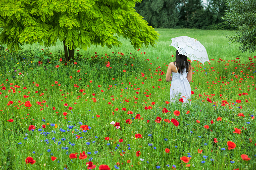Young woman in white sun dress with umbrella in garden.