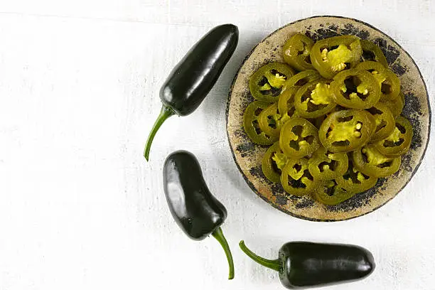 Green fresh and delicious sliced pickled jalapenos on stone with wooden background