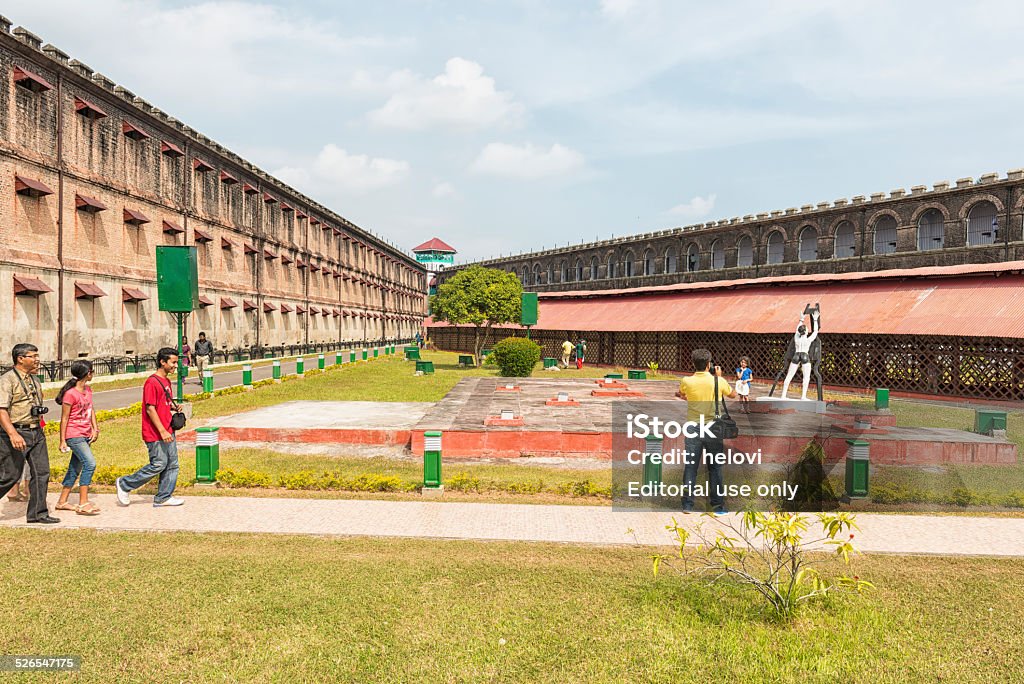 Cellular Jail Andaman Islands Port Blair, India - December 28, 2013: Two three storey wings with a central-tower acting as its fulcrum. On grass in between sculpture of a prisoner on pillar suffering. Small group of tourists walking on path and taking photos. Prison Stock Photo