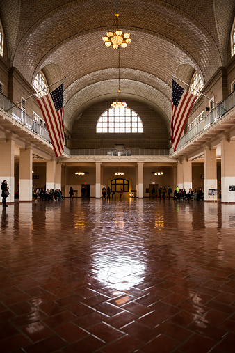 New York, USA - November 16, 2014: Early in the morning at the Iconic Registry Room on Ellis island with tourists passing through the very area their ancestors passed through gaining passage into the United State of America.  