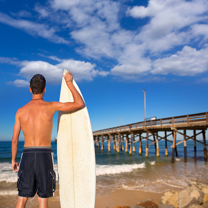 Boy surfer back rear view holding surfboard on Newport pier beach California