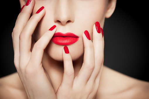 Closeup of face and hands with beautiful manicure and red glossy polish and matte red lipstick.