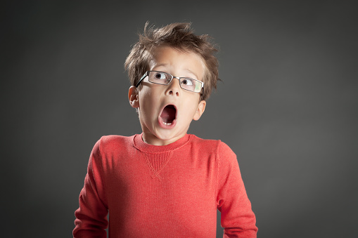 Scared and shocked little boy in glasses. Studio shot portrait over gray background. Fashionable little boy.