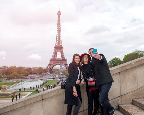 Portrait of friends using smartphone to take self portrait near the Eiffel Tower.