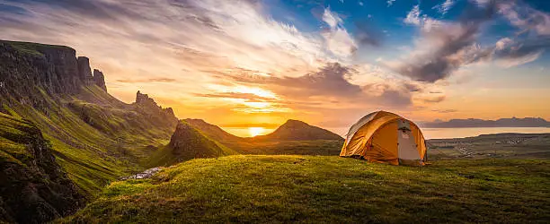 Dome tent illuminated by the warm glow of sunrise as a golden cloudscape reveals the dramatic mountain pinnacles of this panoramic landscape. ProPhoto RGB profile for maximum color fidelity and gamut.