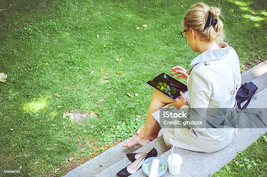 Young businesswoman on a lunch break in park Rear view of a young barefoot businesswoman on a break outdoors. Young professional business woman using tablet computer during her lunch break in park. Copy space has been left. Grass Stock Photo