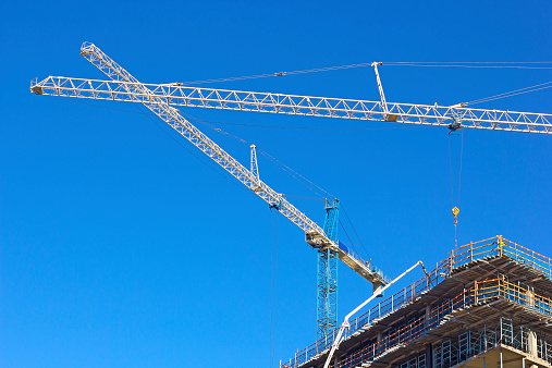 Construction cranes against a clear blue sky.