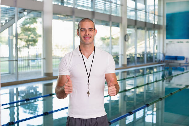 Swimming coach with a wistle and stopwatch posing inside an indoor swimming pool