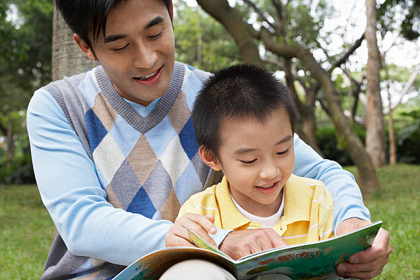 istock Father And Son Reading Book In Park 526597971