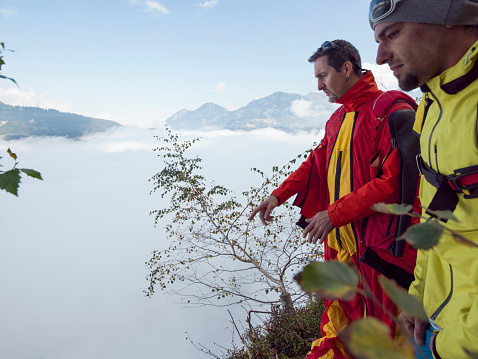BASE/Wing suit fliers ponder landing before jumping from cliff, mountains & fog behind