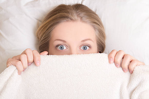 funny young woman lying in bed under blanket stock photo