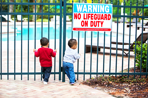Two toddler boys are attempting to enter an unlocked gate at a large swimming pool at a resort..  Shot with Canon 5D Mark 3  rr