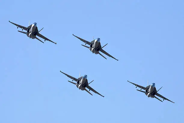 Formation of four F/A-18 fighter aircraft flying against a blue sky
