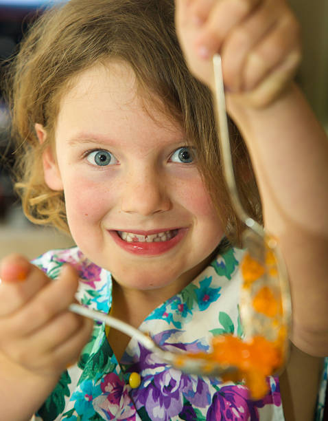 Young child making jelly with broad smile and two spoons.