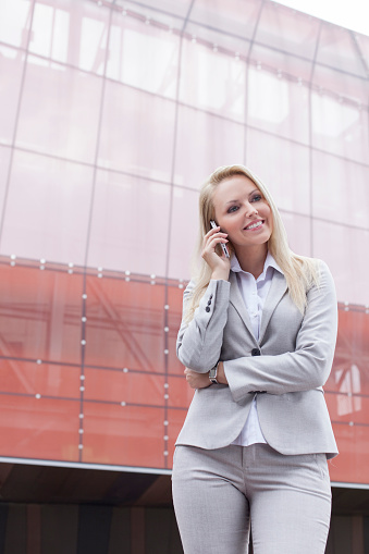 Beautiful young businesswoman using mobile phone while standing against office building