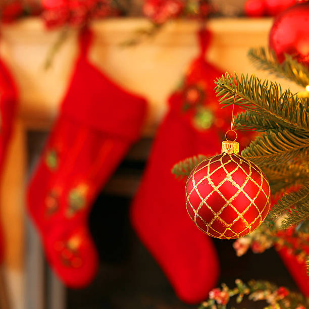 Focus on the Christmas ball. Mantelpiece with Christmas stockings in the background.