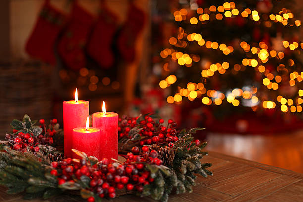 Christmas wreath with burning candles. Blur Christmas tree lights in the background.