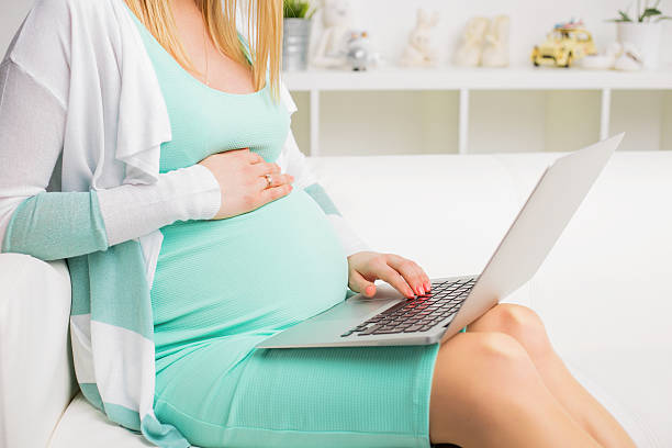 istock Pregnant woman sitting on couch and using laptop 526713740