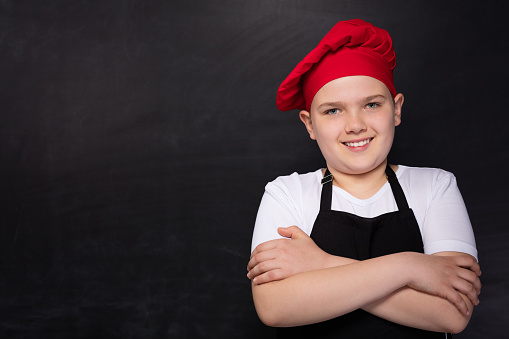 Chef child posing at camera on red background.
