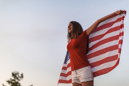Young smiling hipster girl at the beach, holding American flag