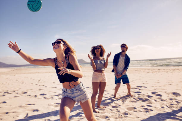 Friends playing beach volleyball Group of friends playing volleyball on the sandy beach and having fun. Young people on summer holidays playing with ball on the beach. beach volleyball stock pictures, royalty-free photos & images