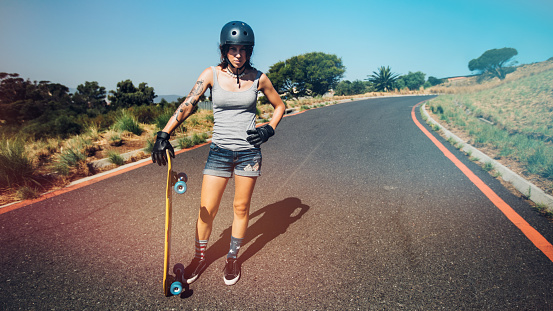 Full length portrait of young woman standing on a countryside highway with a longboard.
