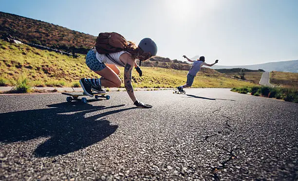 Young people skateboarding outdoors on the road. Young man and woman practicing skating on a rural road.