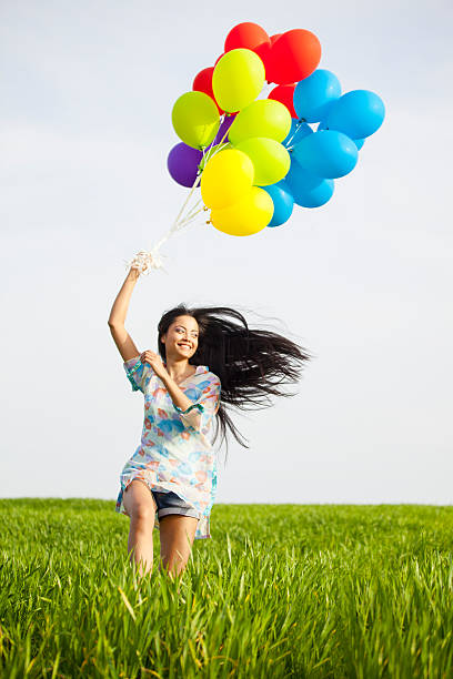 smiling young woman with brunch of balloons running in grassland-close-up - china balloon 個照片及圖片檔