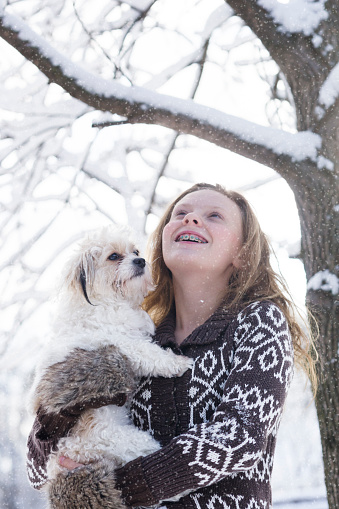 Blond girl with her little white Ocherese dog watch a fresh snowfall outdoors on a snowy day