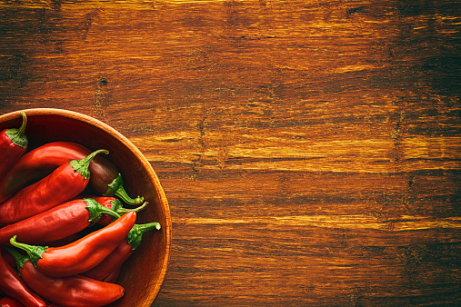 Red chili peppers fill a wooden bowl on wood cutting board