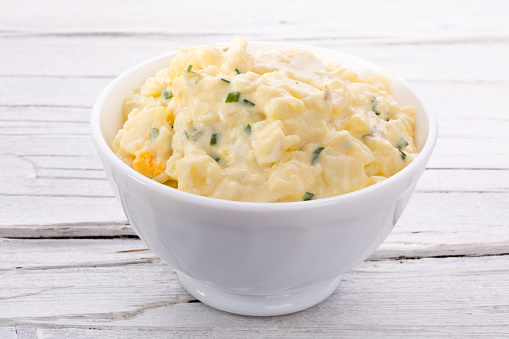 potato salad in white bowl on white wooden background