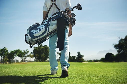 Golf man walking with shoulder bag on course in fairway