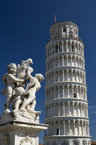 Statue And Leaning Tower Of Pisa (Italy). Blue sky in the background.