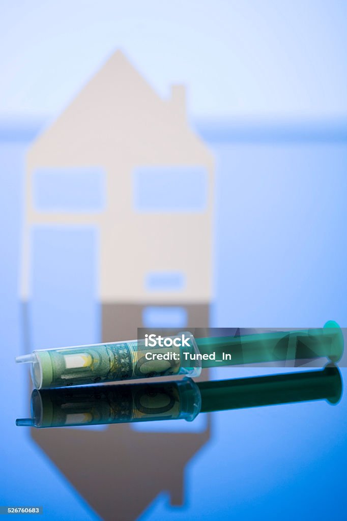 100 Euro banknote wrapped in syringe, Model house in background Bank Account Stock Photo