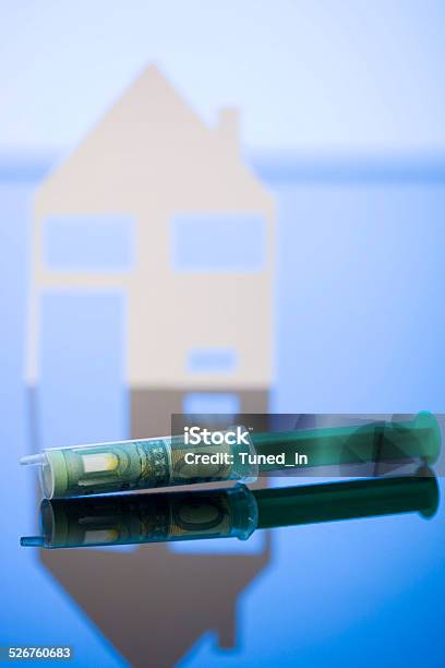 100 Euro Banknote Wrapped In Syringe Model House In Background Stock Photo - Download Image Now