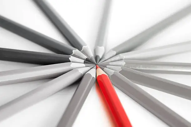 Bright red pencil standing out among gray pencils, concept of thinking differently and out of the box. On a white background with soft focus.