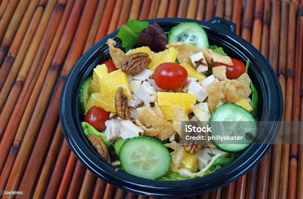 Thai Chicken Salad Thai chicken salad with walnuts, cucumbers, tomatoes, oranges and crispy noodles in a takeout bowl on bamboo mat. Bowl Stock Photo