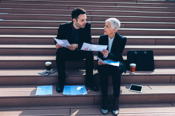 istock Businesspeople sitting on stairs and examining paperwork. 526823026